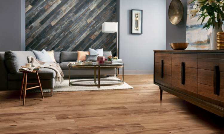 warm toned wood look flooring in living room with grey couch and gold and blue accents